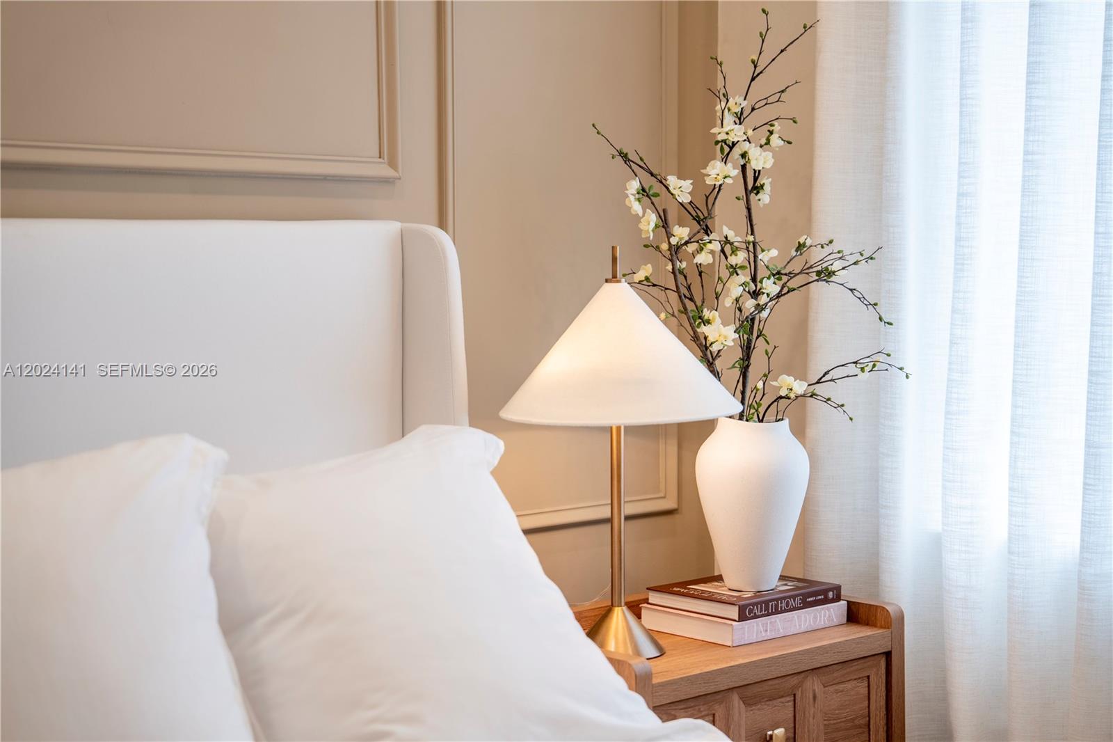 A bedside table with a lamp and floral arrangement sits next to a white headboard — DORAL, FL