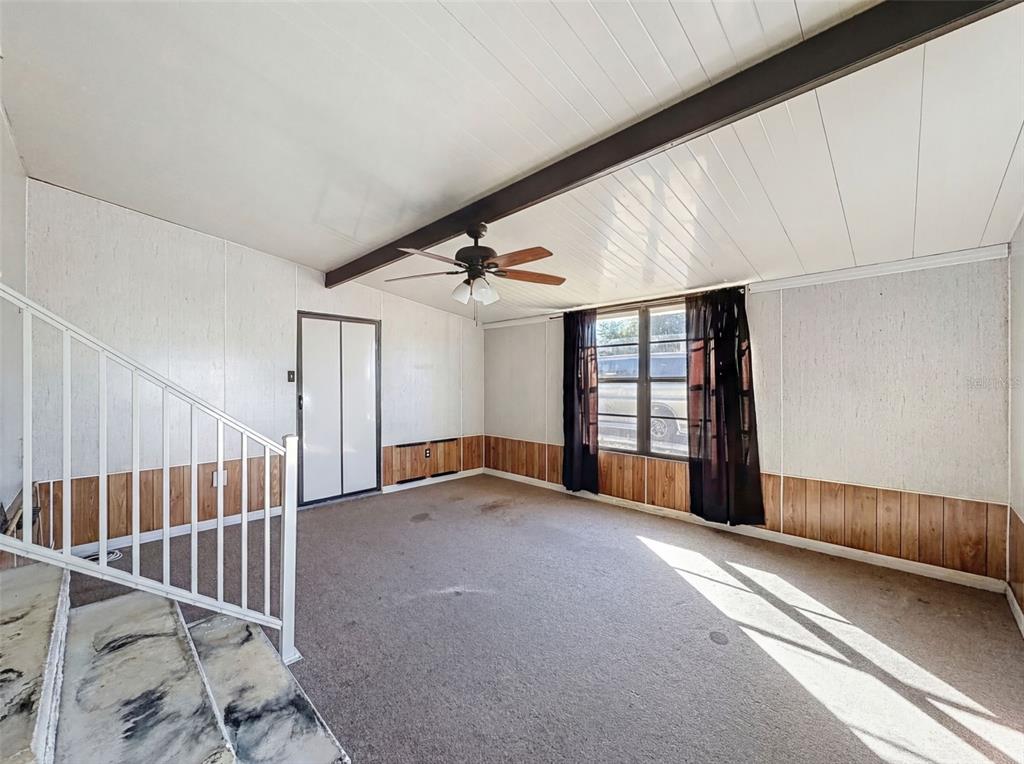 A room with wood-paneled wainscoting, carpeted flooring, a ceiling fan, and a staircase — 12304 LONGHORN DRIVE, HUDSON, FL