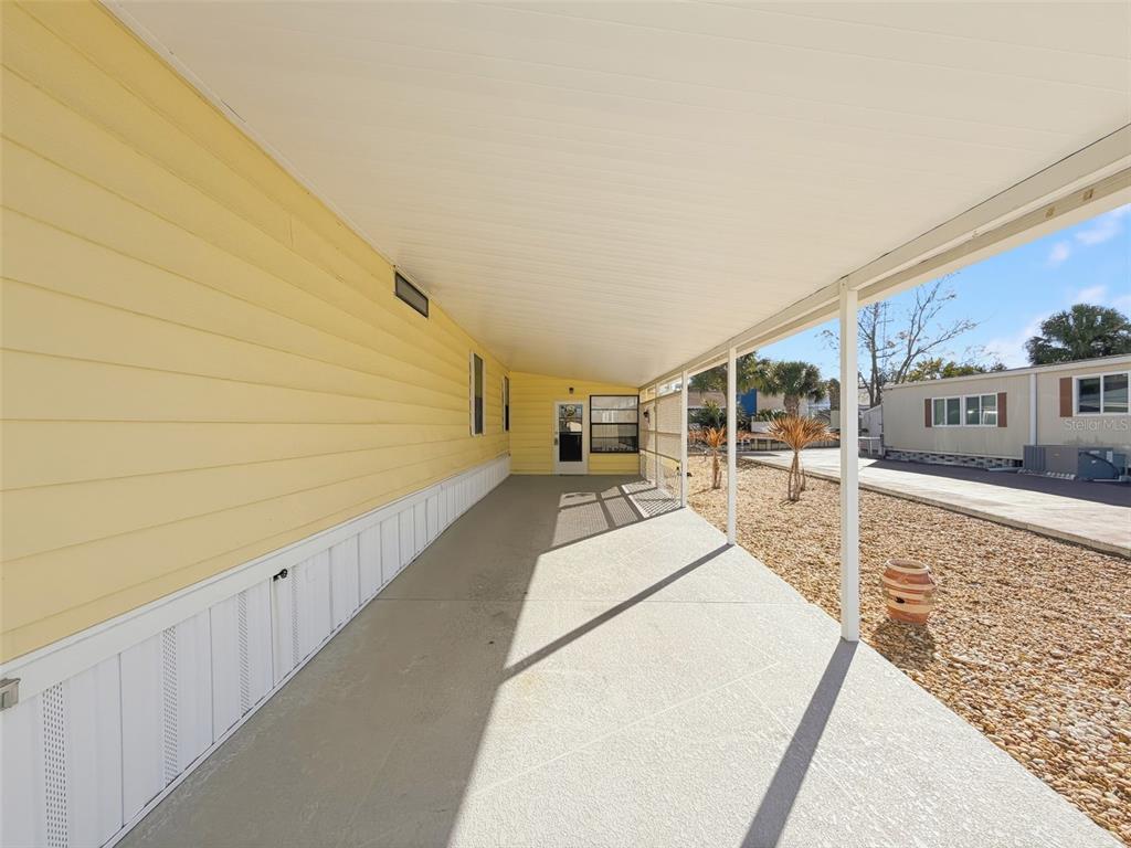 A covered concrete patio runs alongside a yellow mobile home with white skirting — 12304 LONGHORN DRIVE, HUDSON, FL