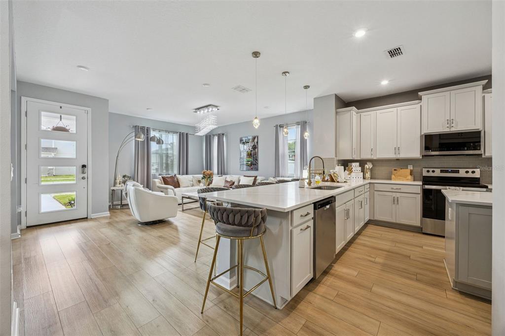 An open-concept kitchen and living area featuring light wood floors, white cabinets, and an island — 11492 SUNSAIL AVENUE, ORLANDO, FL