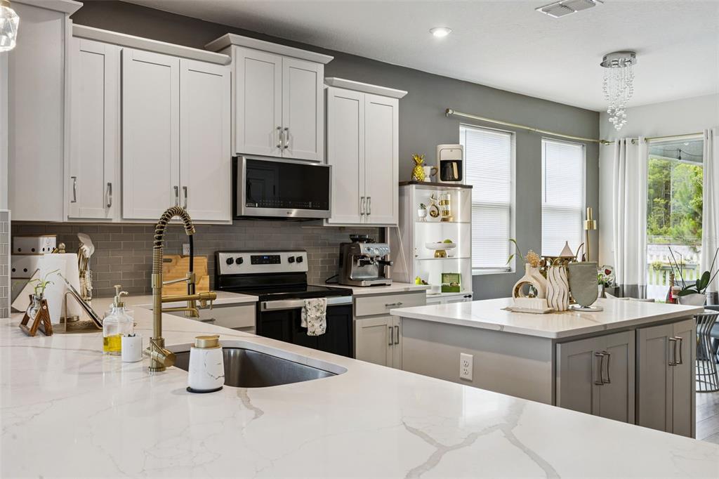 A modern kitchen features white cabinetry, a marble-patterned island, and a gold-toned faucet — 11492 SUNSAIL AVENUE, ORLANDO, FL