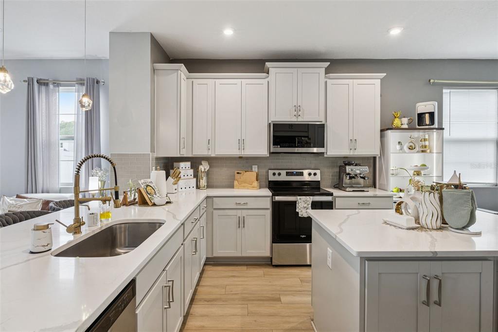 A modern kitchen features white cabinetry, quartz countertops, stainless steel appliances, and wood-look flooring — 11492 SUNSAIL AVENUE, ORLANDO, FL