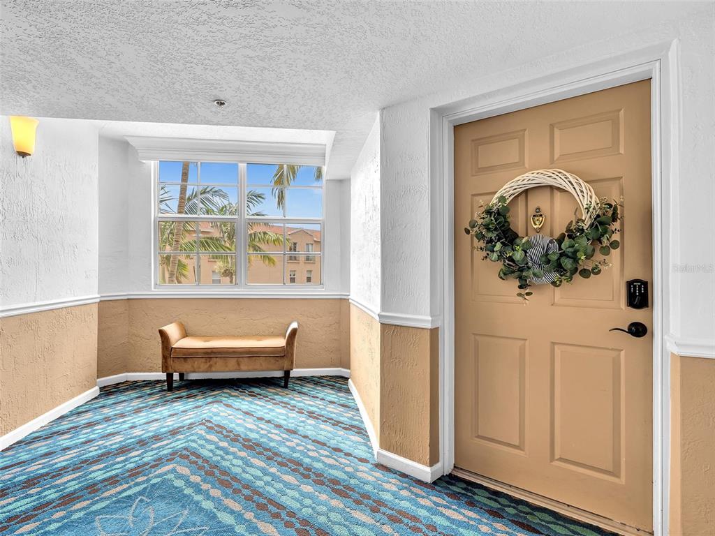 A carpeted hallway features a tan bench, a window with exterior views, and a door — 1801 N FLAGLER DRIVE UNIT 416, WEST PALM BEACH, FL