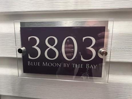 A rectangular sign with the number 3803 and text mounted on a white siding wall — 3803 116TH STREET COURT W, BRADENTON, FL