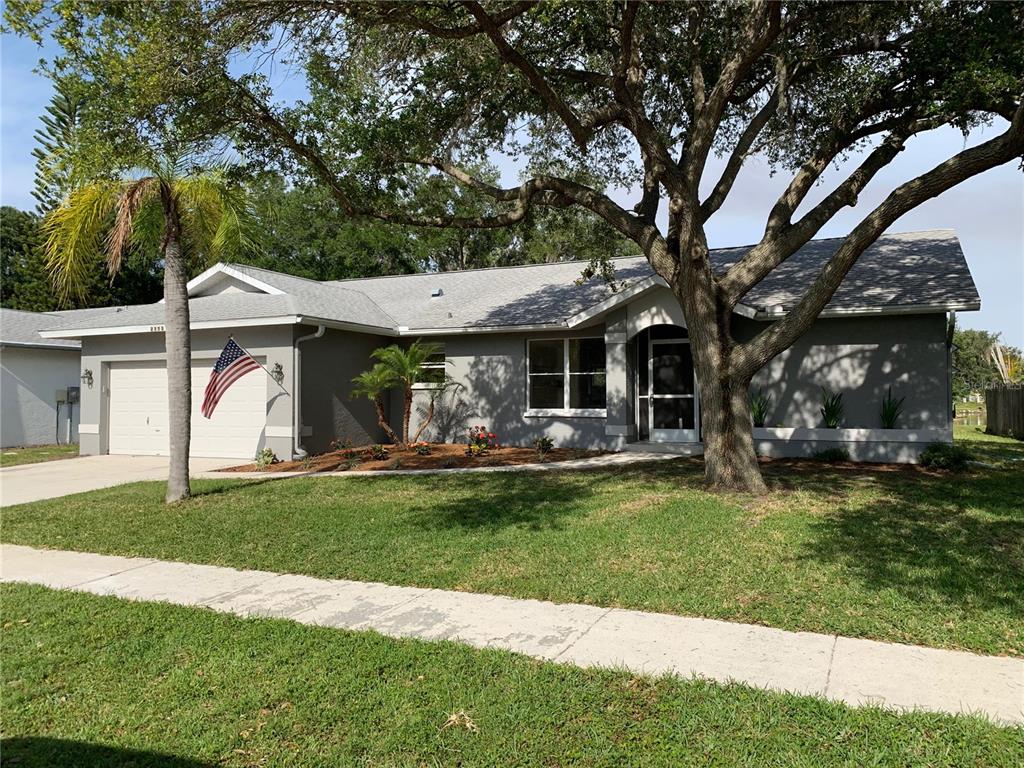 A single-story gray house with a two-car garage, a large oak tree, and a lawn — 2193 CORK OAK STREET E, SARASOTA, FL