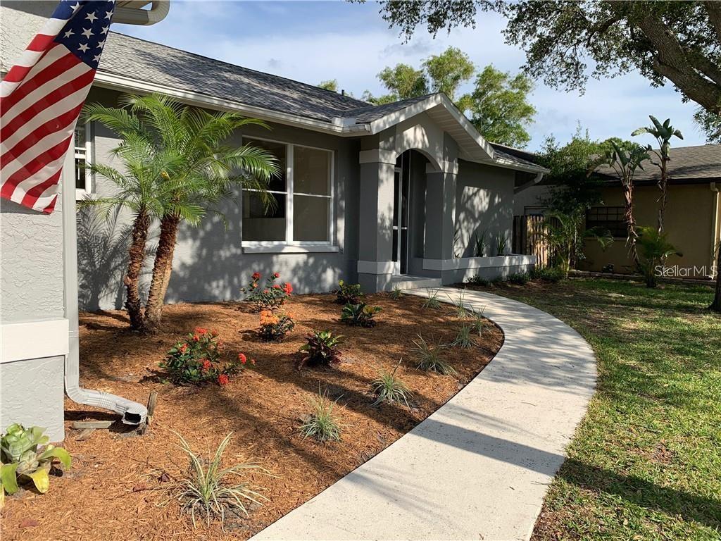 A gray house exterior features a curved concrete walkway, palm trees, and a front porch — 2193 CORK OAK STREET E, SARASOTA, FL