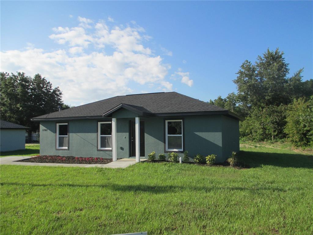 A single-story green house with a dark shingled roof stands on a grassy lot — 5762 NW 5TH STREET, OCALA, FL