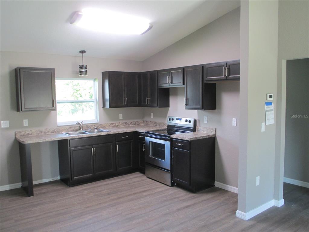 A kitchen features dark wood cabinets, laminate countertops, stainless steel appliances, and wood-look flooring — 5762 NW 5TH STREET, OCALA, FL
