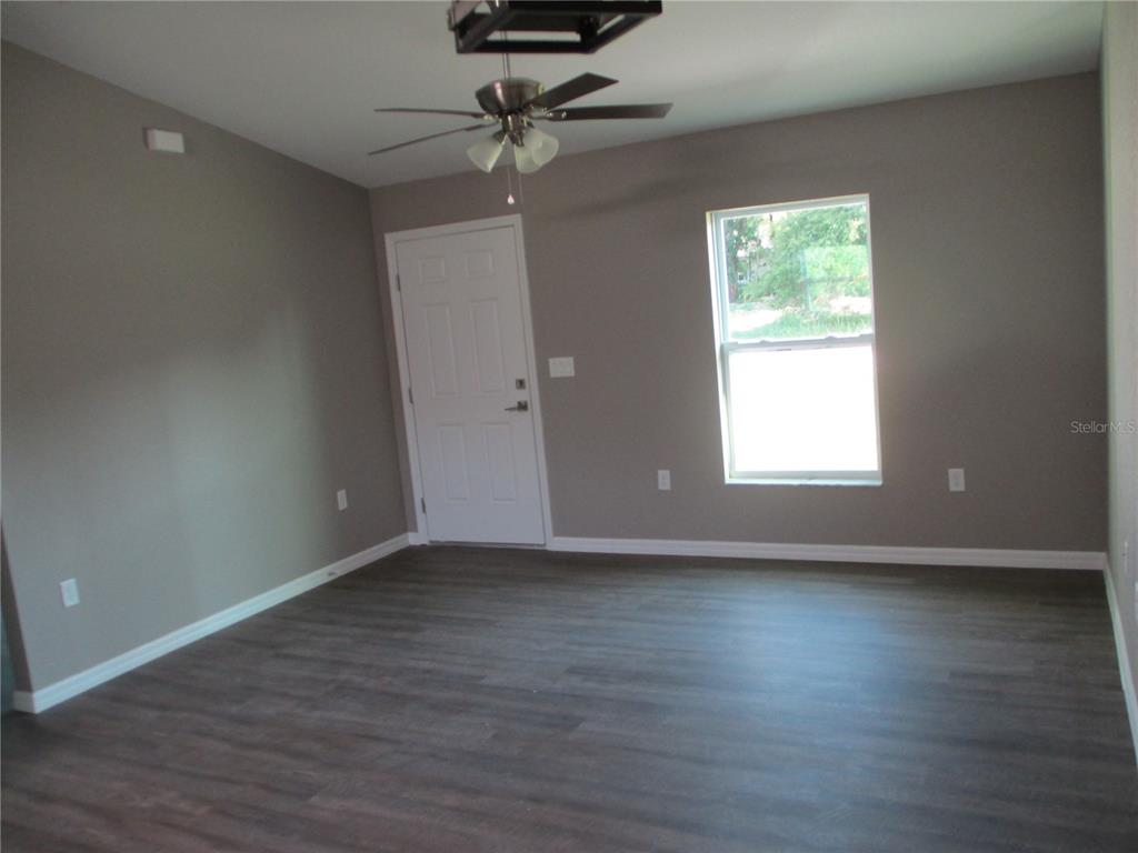 An empty room features gray walls, dark wood-look flooring, a ceiling fan, and a door — 5762 NW 5TH STREET, OCALA, FL