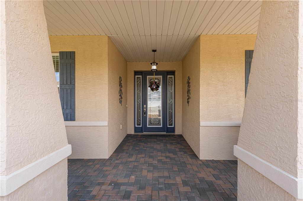 A covered entryway features a dark blue front door with glass panels and paver flooring — 9041 SW 88TH PLACE, OCALA, FL