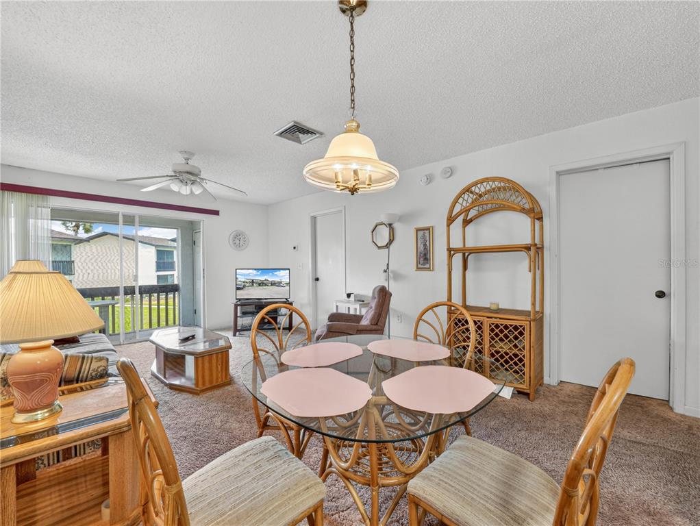A dining area with a glass table and rattan chairs sits adjacent to a living space — 900 AVENUE Z SE UNIT D6, WINTER HAVEN, FL