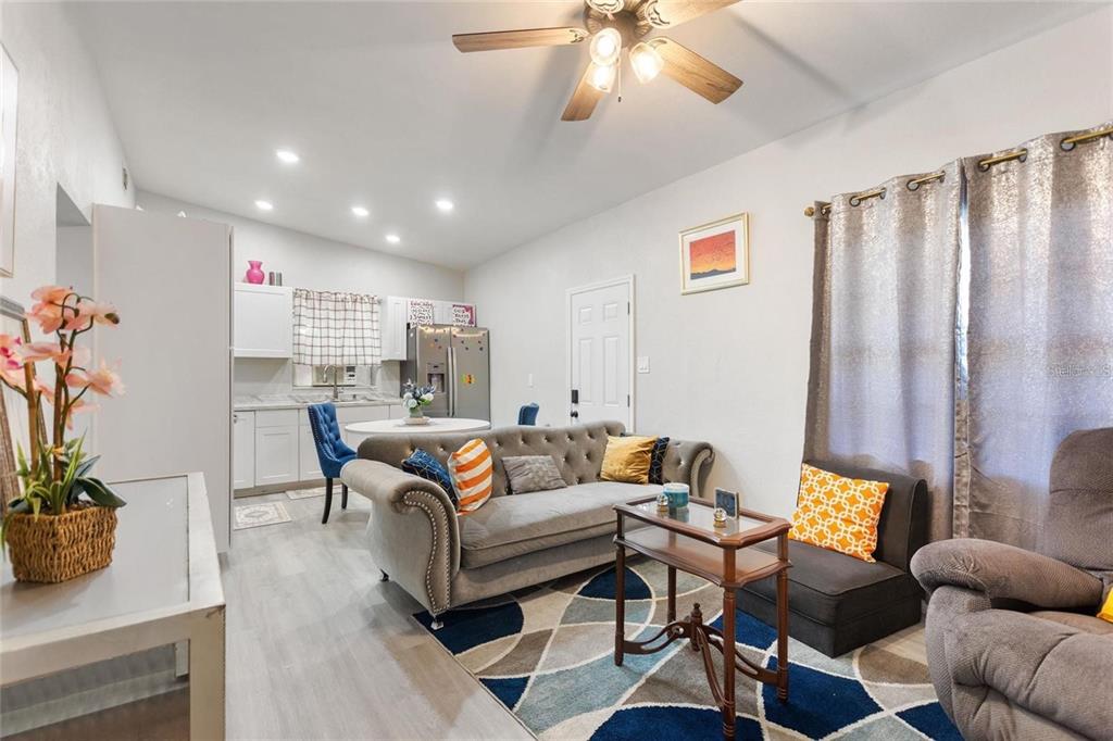 A living room with a grey tufted sofa, patterned rug, and an adjacent kitchen area — 1495 PENNIWA STREET, INTERCESSION CITY, FL