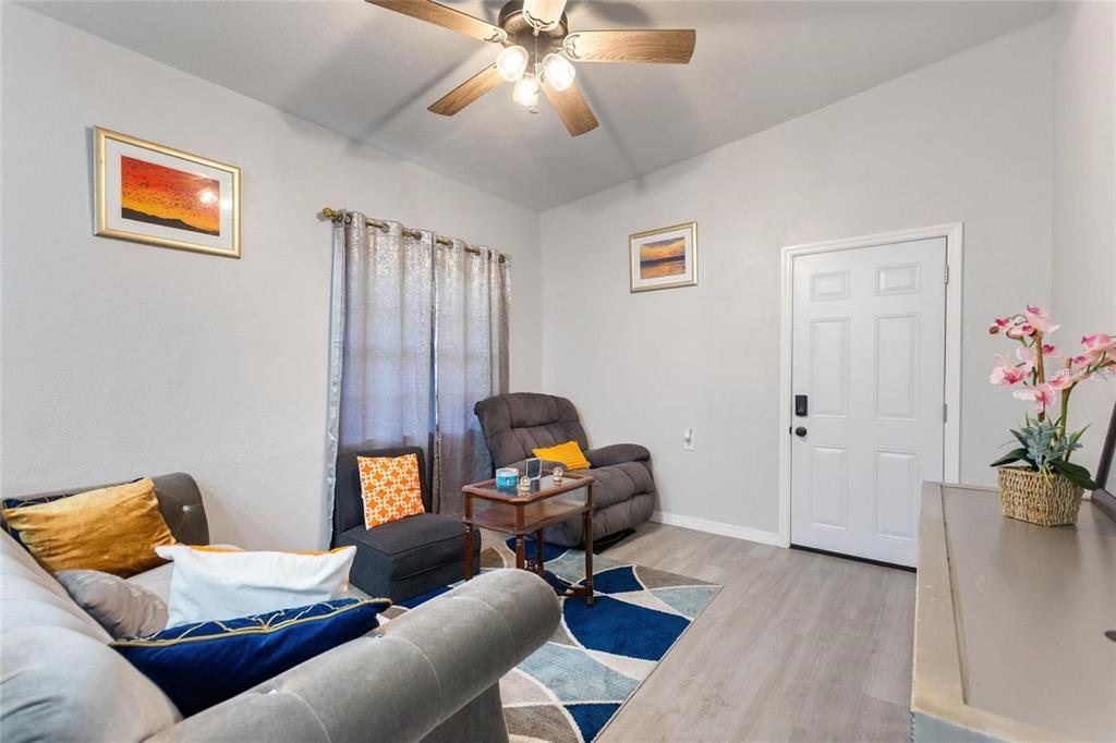 A living room features gray walls, light wood-look flooring, a ceiling fan, and a door — 1495 PENNIWA STREET, INTERCESSION CITY, FL