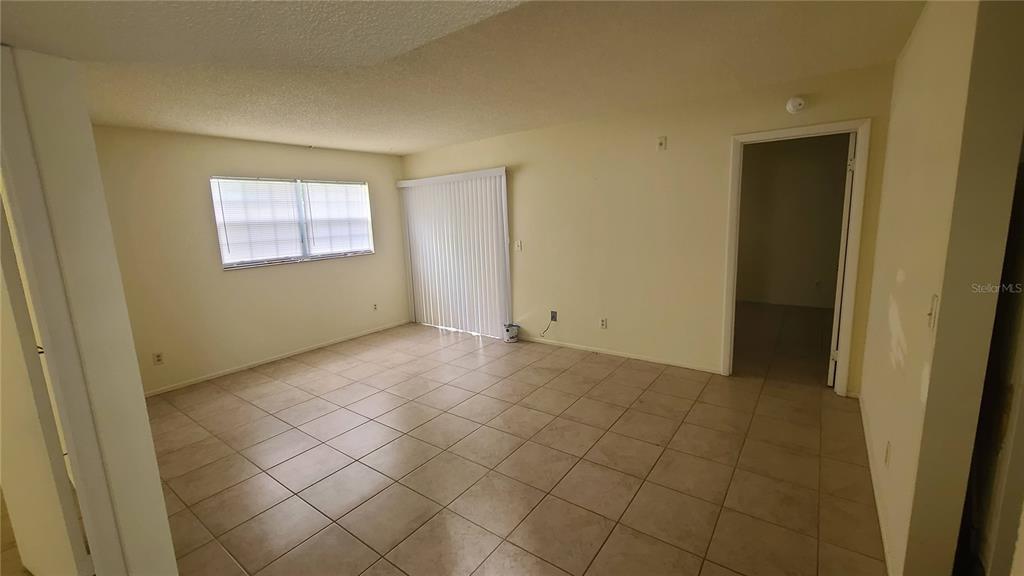 An empty room features beige tile flooring, white walls, a window, and sliding glass doors — 454 FAIRWAYS CIRCLE UNIT B102, OCALA, FL