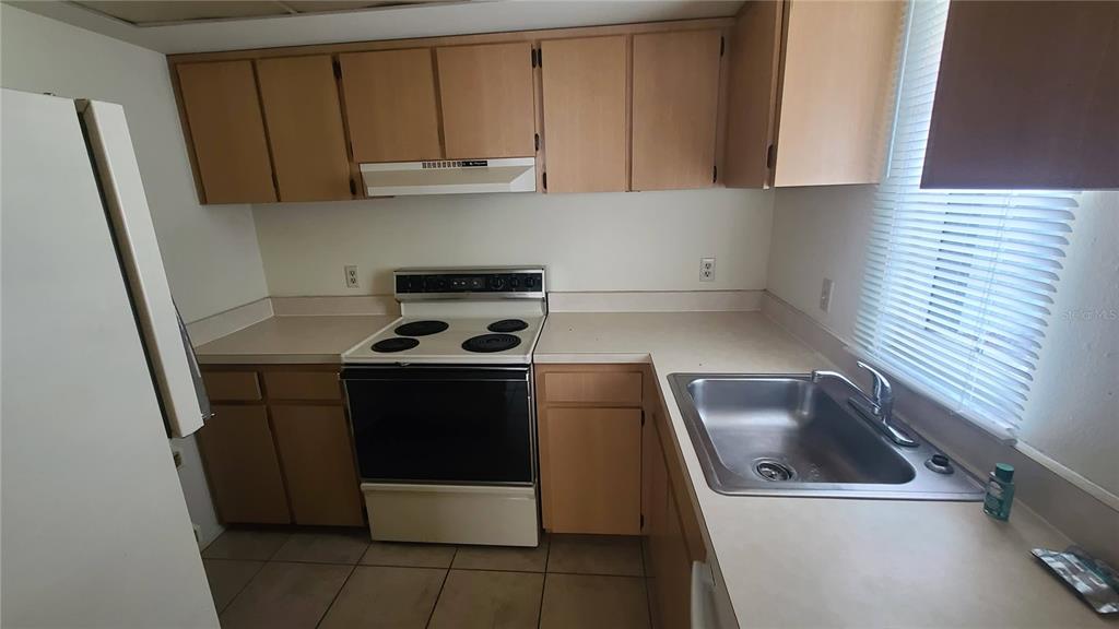 A kitchen features light wood cabinets, white appliances, a stainless steel sink, and tiled flooring — 454 FAIRWAYS CIRCLE UNIT B102, OCALA, FL