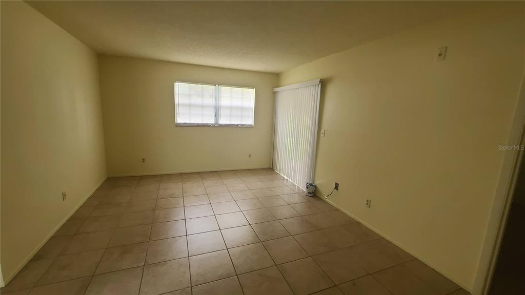 An empty room features beige walls, light-colored tile flooring, a window, and sliding glass doors — 454 FAIRWAYS CIRCLE UNIT B102, OCALA, FL