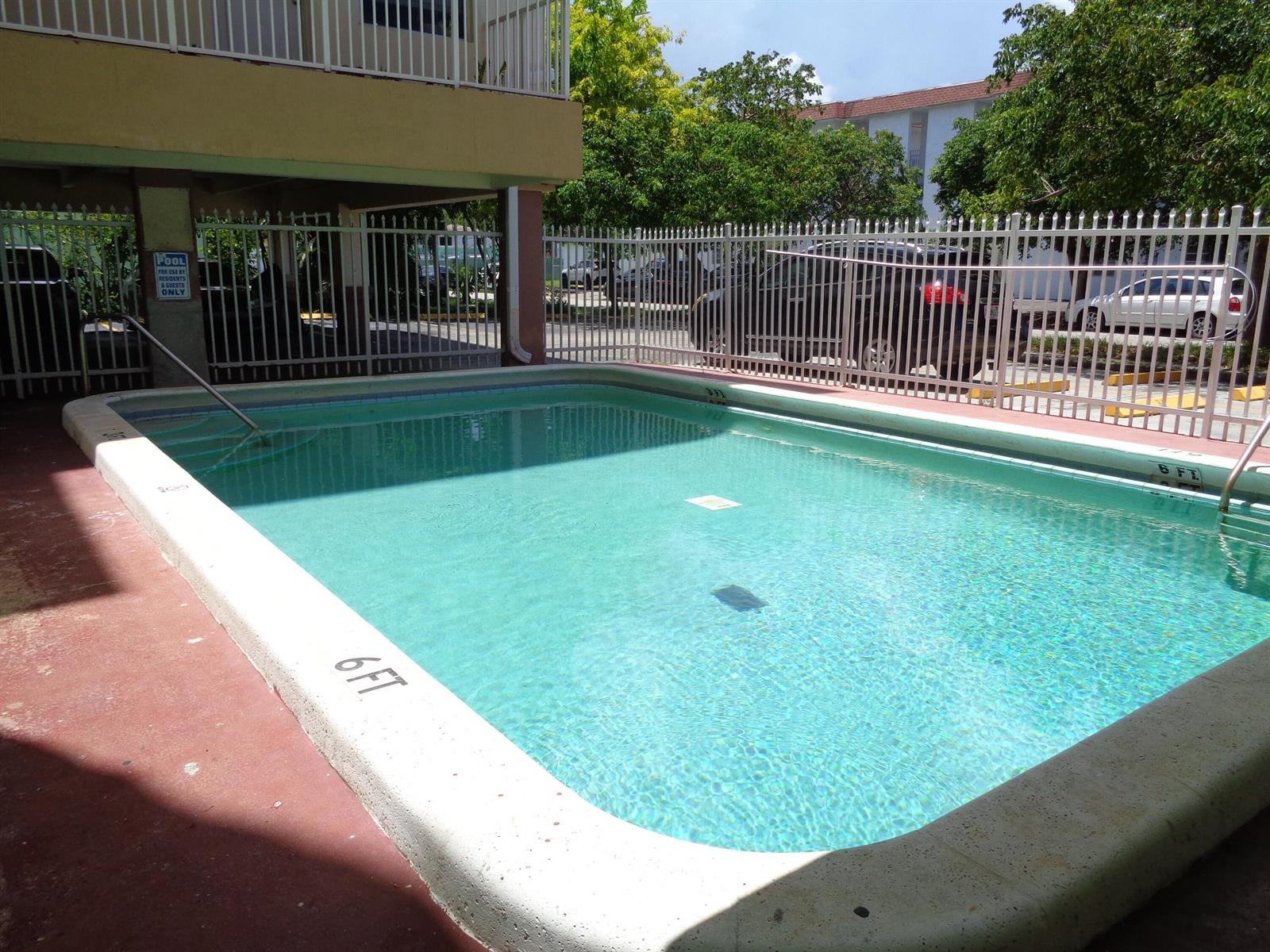 A rectangular outdoor swimming pool is enclosed by a white metal fence — 2008 Jackson Street # E9, Hollywood FL 33020, HOLLYWOOD, FL