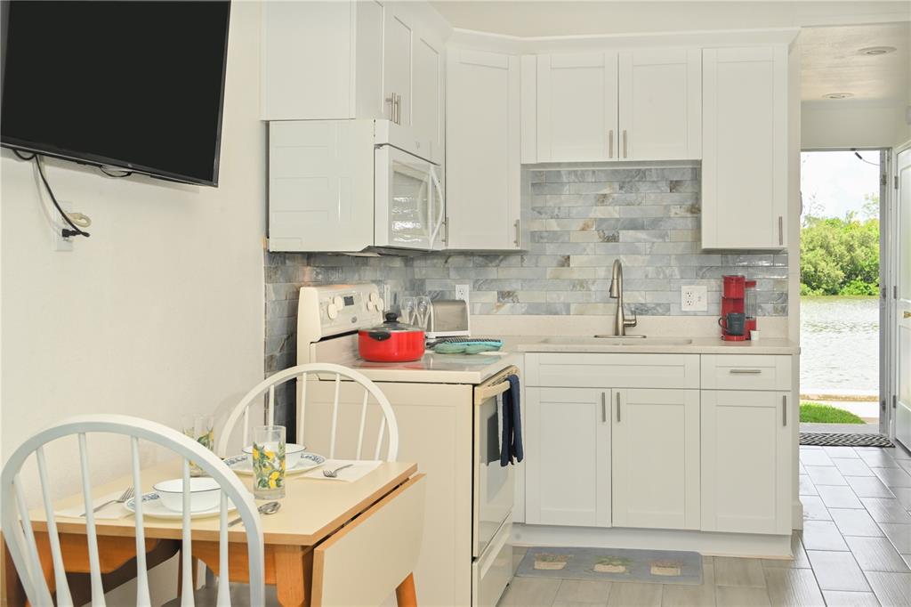 A small kitchen with white cabinets, a tiled backsplash, and a view of the water — 18399 GULF BOULEVARD UNIT 371, INDIAN ROCKS BEACH, FL