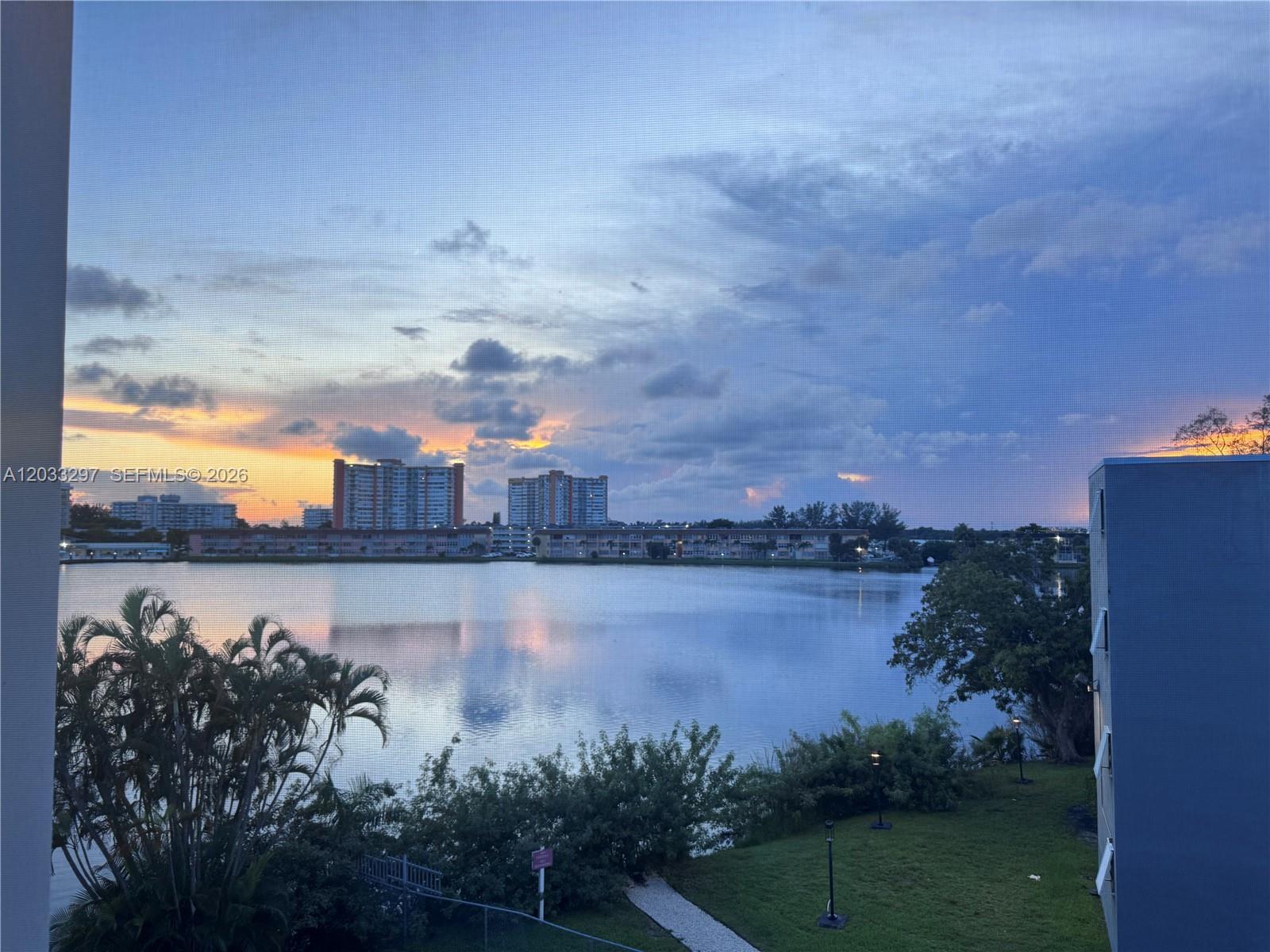 A view of a lake and apartment buildings at sunset from behind a screen — 1660 NE 191st St # 1, Miami FL 33179, MIAMI, FL