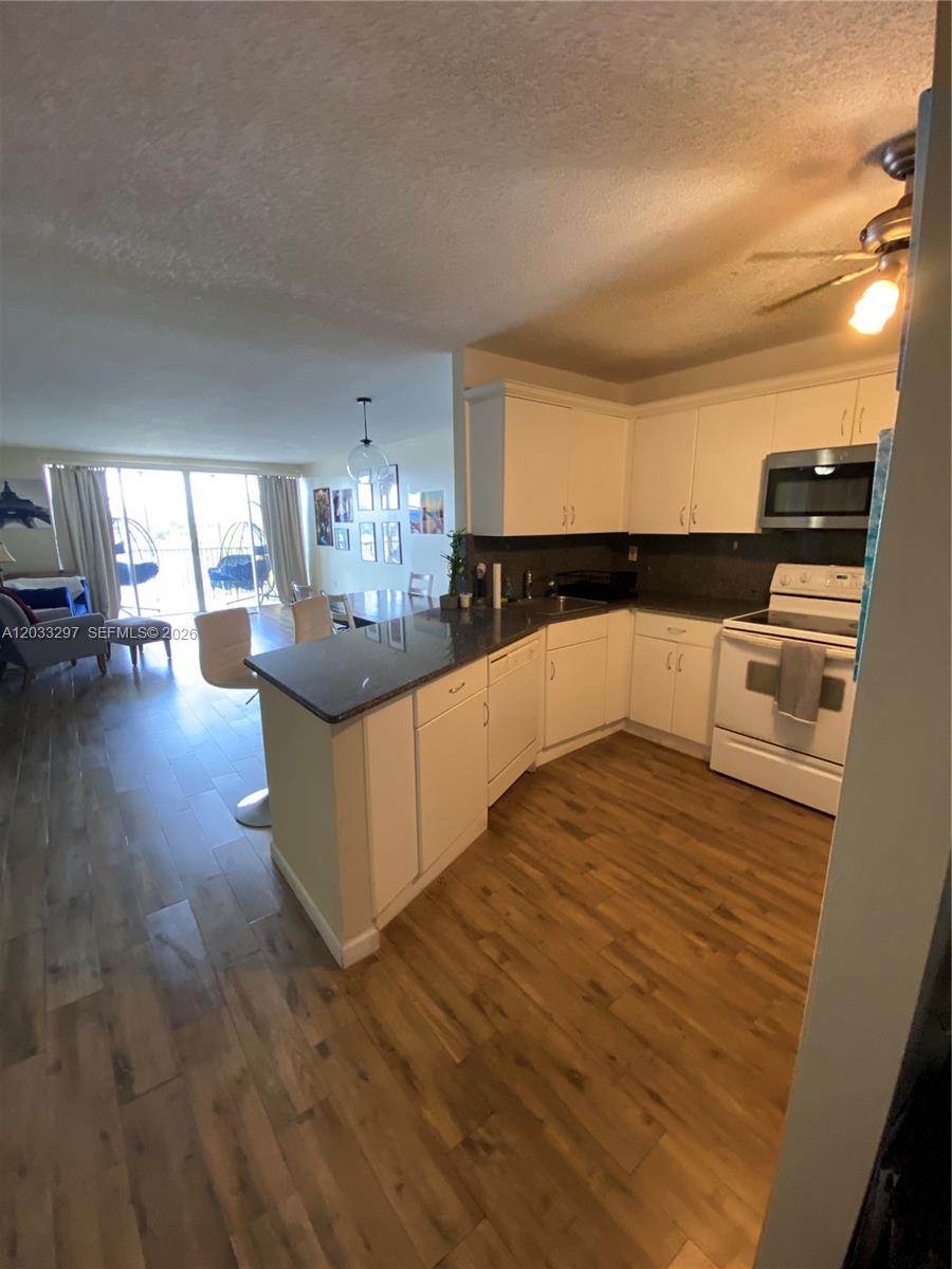 A kitchen with white cabinets and dark countertops opens into a living area with balcony access — 1660 NE 191st St # 1, Miami FL 33179, MIAMI, FL