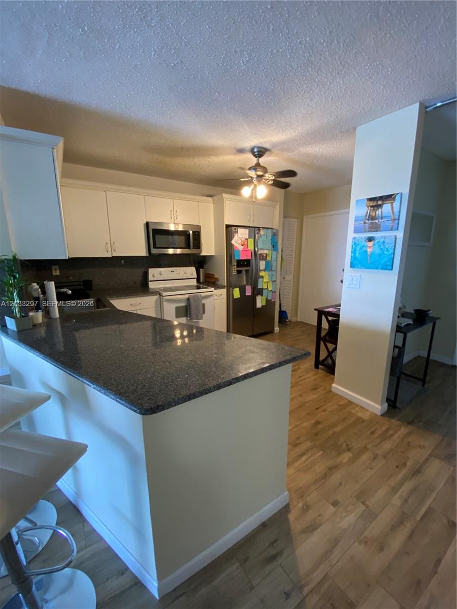 A kitchen features white cabinets, stainless steel appliances, and a granite-topped peninsula island — 1660 NE 191st St # 1, Miami FL 33179, MIAMI, FL