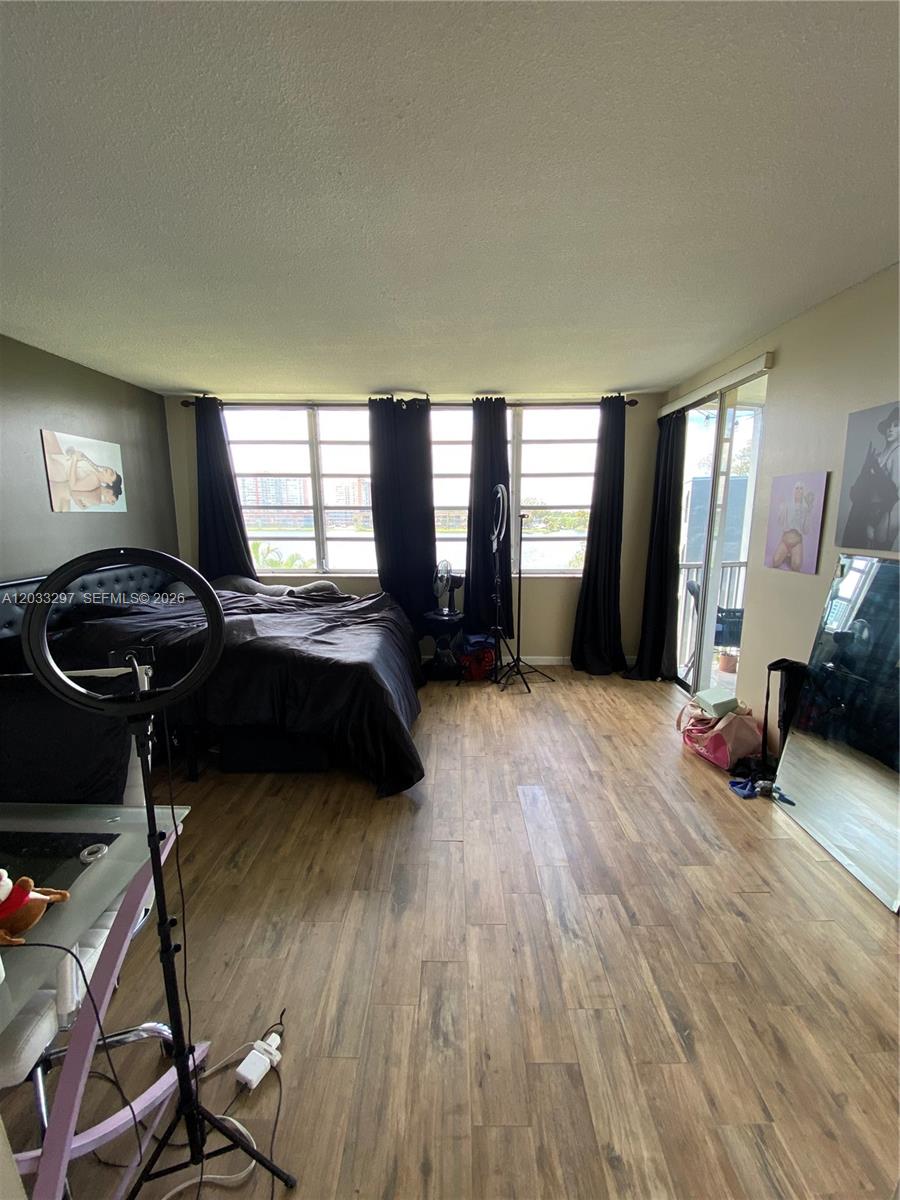 A bedroom with wood-look flooring, a bed, black curtains, and a sliding glass door — 1660 NE 191st St # 1, Miami FL 33179, MIAMI, FL