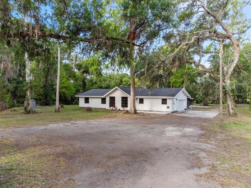 A white, single-story house with a dark roof sits on a large, wooded dirt lot — 6005 IKE SMITH ROAD, PLANT CITY, FL