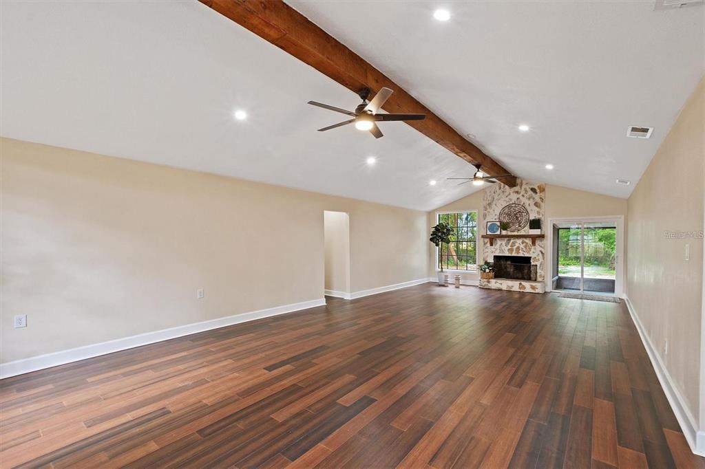 A spacious living room features wood-look flooring, a vaulted ceiling with exposed beams, and a fireplace — 6005 IKE SMITH ROAD, PLANT CITY, FL