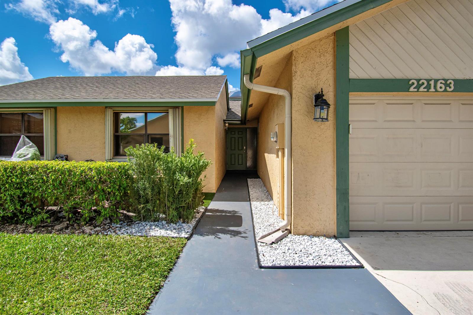 A tan house exterior features a front walkway, a garage, and a green-trimmed roof — 22163 Thomas Terrace, Boca Raton FL 33433, BOCA RATON, FL