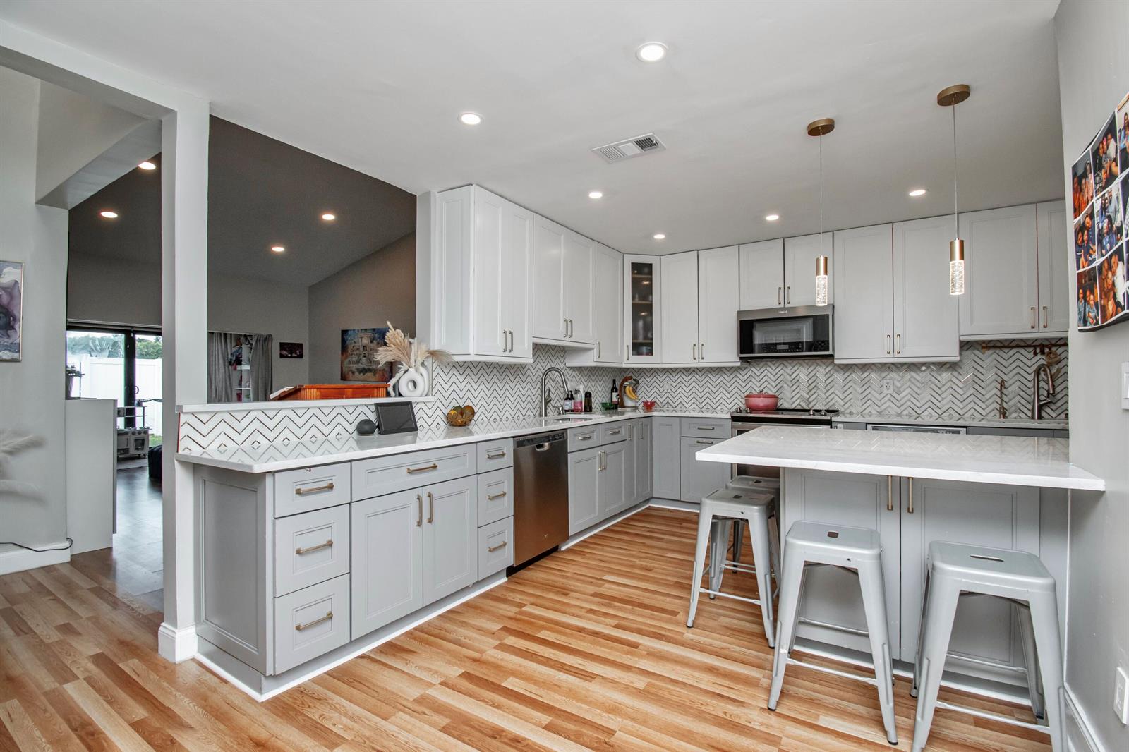 A modern kitchen features light gray cabinets, white countertops, a herringbone backsplash, and wood flooring — 22163 Thomas Terrace, Boca Raton FL 33433, BOCA RATON, FL