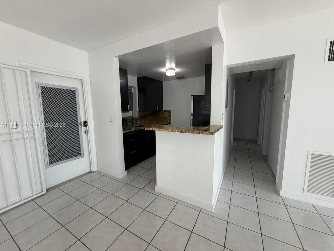A kitchen with dark cabinets and granite countertops opens to a tiled living area — 641 Espanola Way # 3, Miami Beach FL 33139, MIAMI BEACH, FL