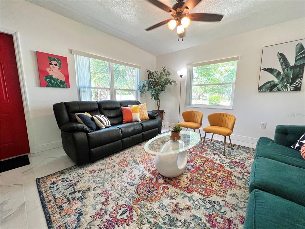A living room features a black sofa, two yellow chairs, and a patterned area rug — 2173 RIVIERA DRIVE, CLEARWATER, FL