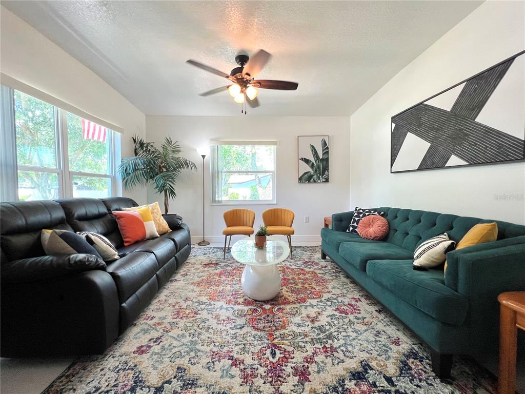 A living room features a black leather sofa, a teal tufted sofa, and a patterned rug — 2173 RIVIERA DRIVE, CLEARWATER, FL