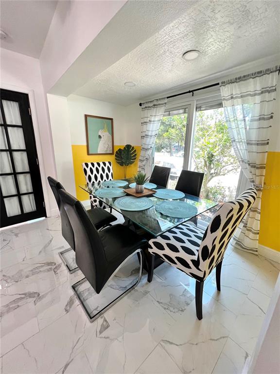 A dining room features a glass table, patterned chairs, and yellow-painted walls with marble flooring — 2173 RIVIERA DRIVE, CLEARWATER, FL