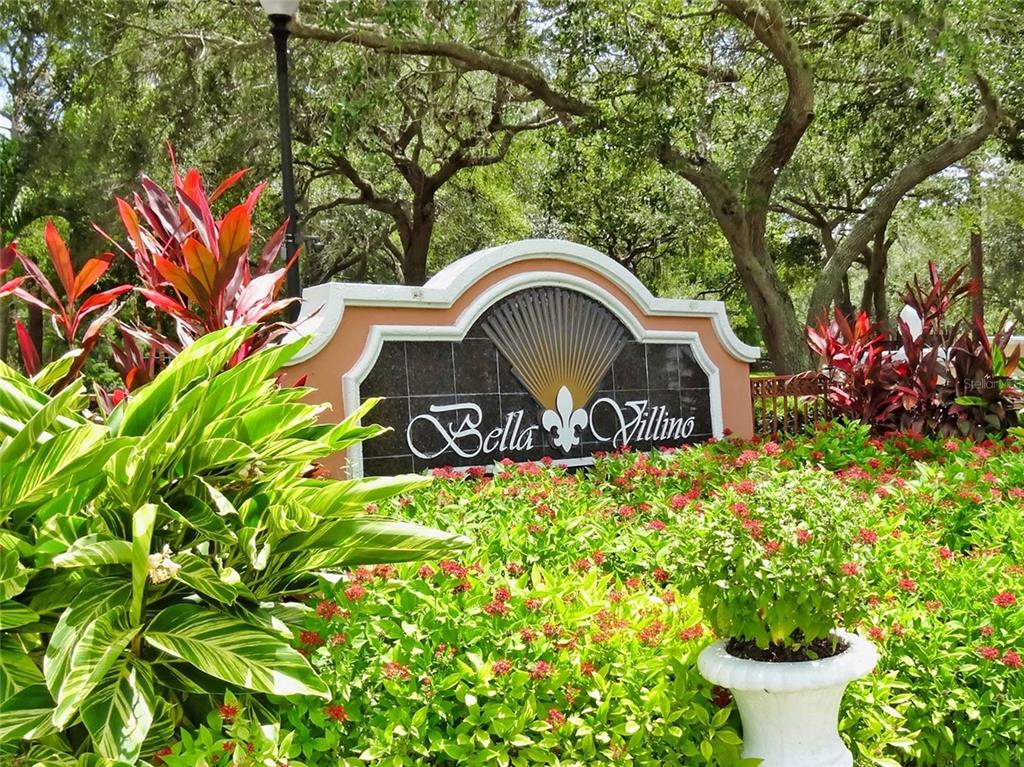 A stone monument sign for Bella Villino sits surrounded by lush landscaping and trees — 4174 CENTRAL SARASOTA PARKWAY UNIT 221, SARASOTA, FL