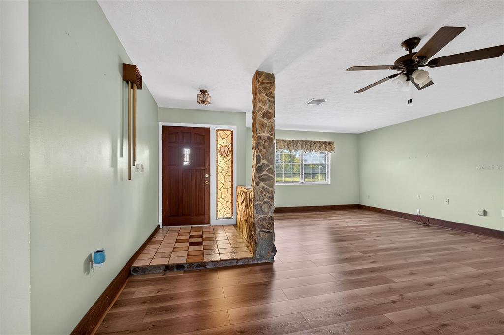 An entryway with a stone pillar and tiled floor transitions into a living room with wood-look flooring — 12776 SE 87TH TERRACE, BELLEVIEW, FL