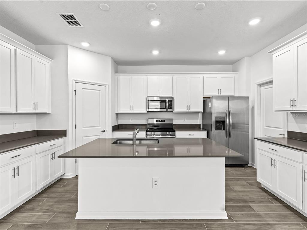 A modern kitchen features white cabinets, a large central island, and stainless steel appliances — 2952 ARMSTRONG AVENUE, CLERMONT, FL