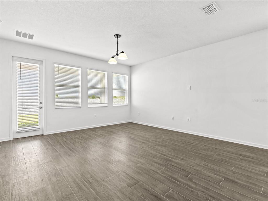 An empty room features wood-look tile flooring, white walls, a hanging light fixture, and windows — 2952 ARMSTRONG AVENUE, CLERMONT, FL