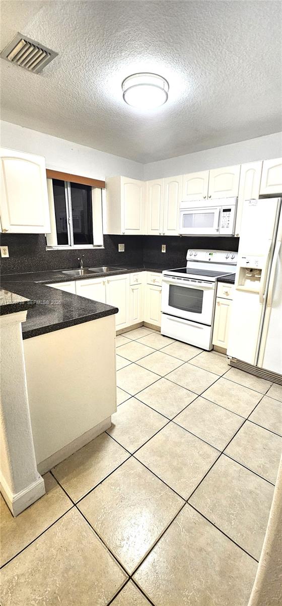 A kitchen features white cabinets, dark countertops, white appliances, and light-colored tile flooring — 7309 NW 173rd Dr # 104, Miami FL 33015, MIAMI, FL