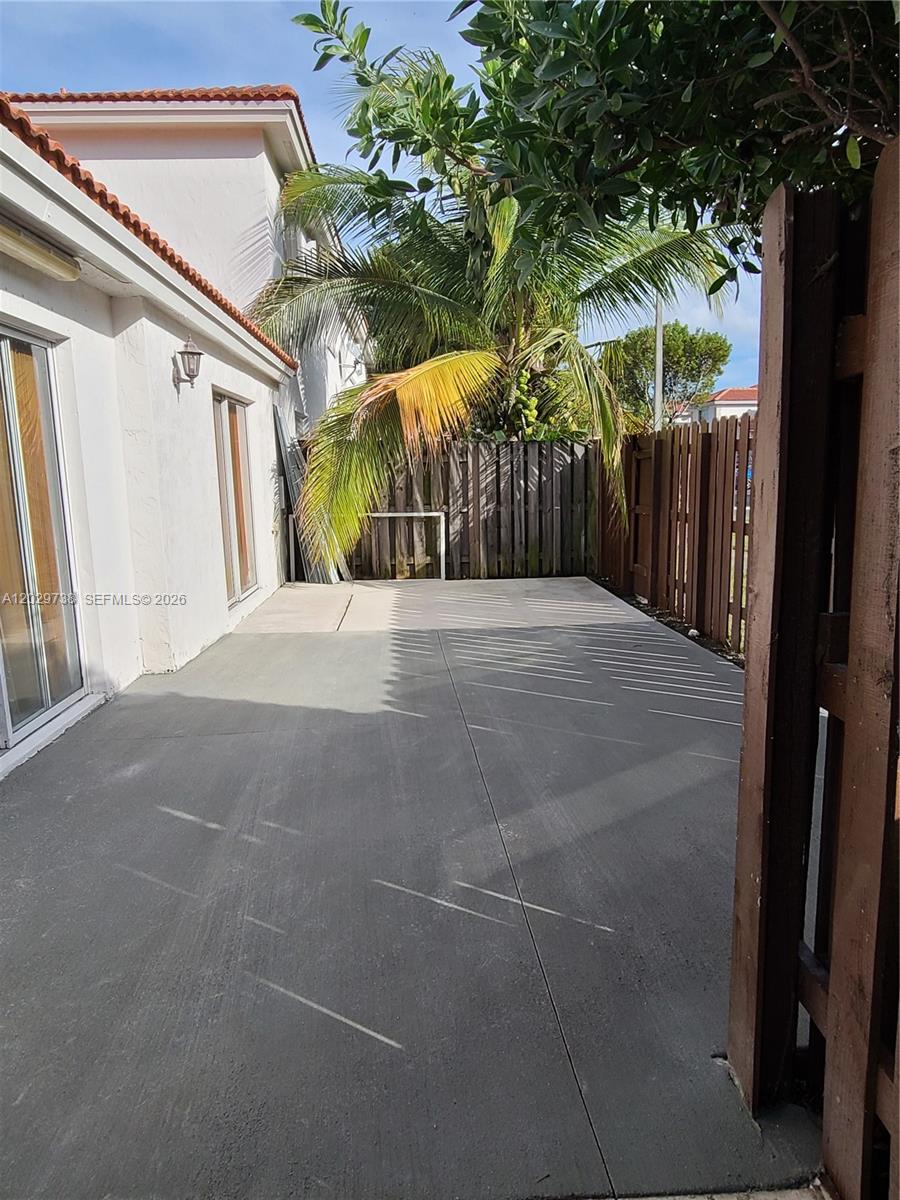 A concrete patio sits beside a white house with a wooden fence and palm tree — 7309 NW 173rd Dr # 104, Miami FL 33015, MIAMI, FL