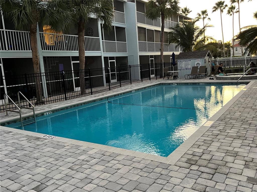 A rectangular swimming pool with a paved deck sits in front of a multi-story apartment building — 751 PINELLAS BAYWAY S UNIT 305, TIERRA VERDE, FL