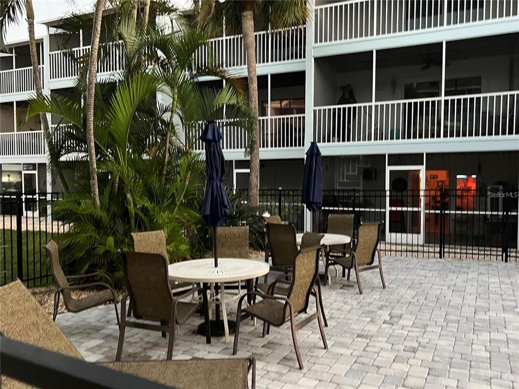 A patio area features outdoor tables and chairs set against a multi-story apartment building — 751 PINELLAS BAYWAY S UNIT 305, TIERRA VERDE, FL