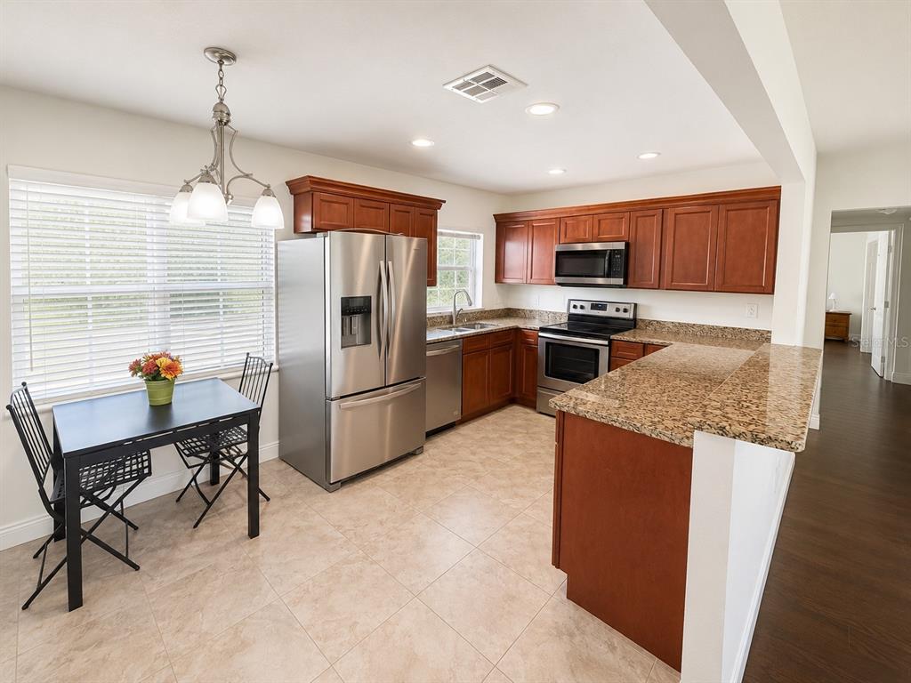 A kitchen with wood cabinets, granite countertops, stainless steel appliances, and a small dining area — 616 ELLENDALE DRIVE, WINTER PARK, FL