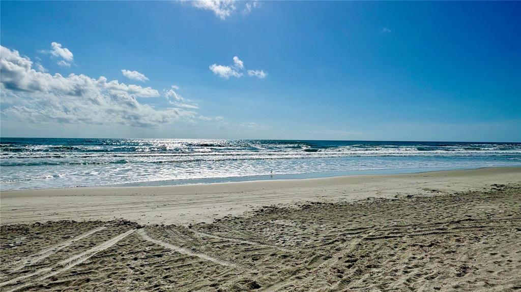 A sandy beach with tire tracks leads to the ocean under a blue sky — 2410 S ATLANTIC AVENUE, NEW SMYRNA BEACH, FL