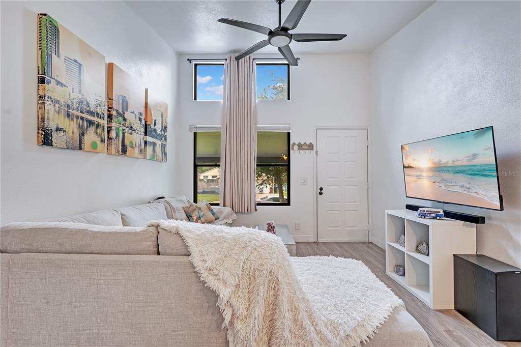 A living room features a sectional sofa, a wall-mounted television, and high ceilings with windows — 415 S LANCELOT AVENUE, ORLANDO, FL