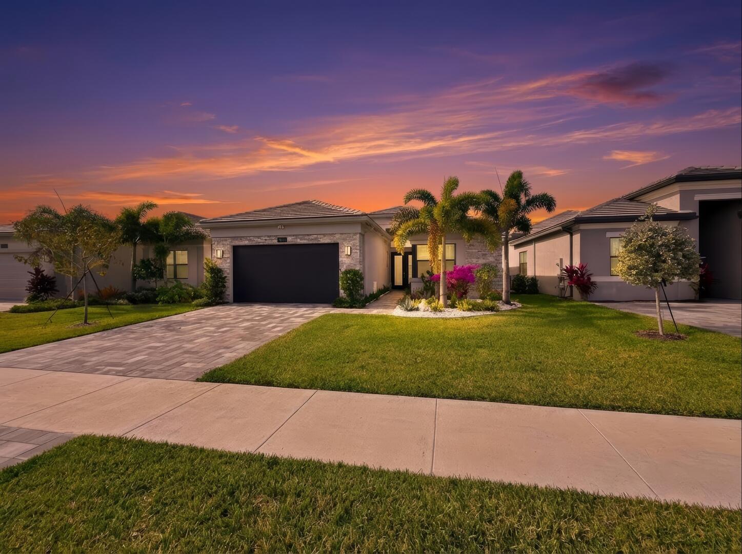 A single-story house with a paved driveway and palm trees under a sunset sky — 9674 Spruce Woods Drive, Boynton Beach FL 33473, BOYNTON BEACH, FL