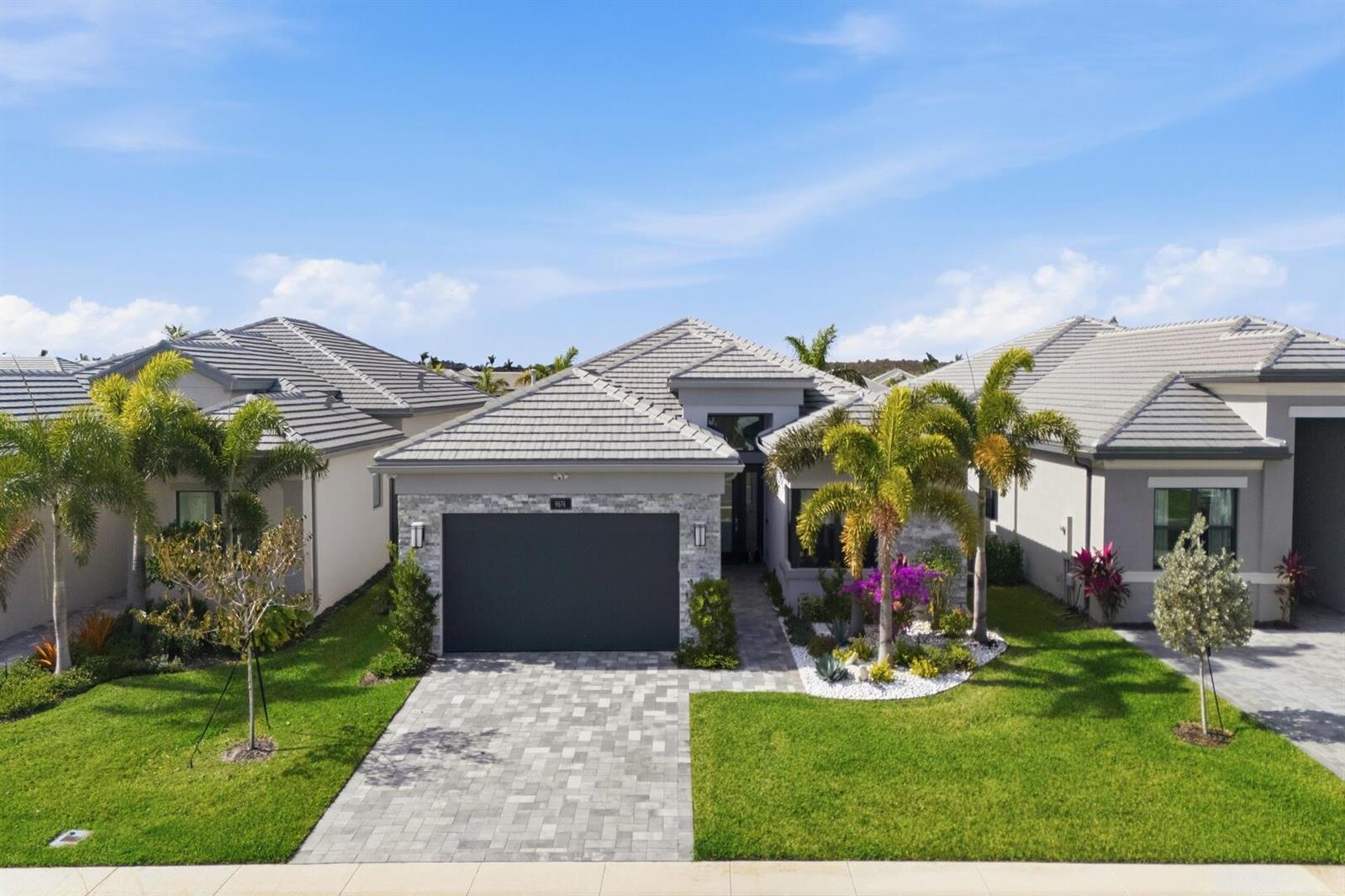 An exterior view of a single-story house with a gray tile roof and stone facade — 9674 Spruce Woods Drive, Boynton Beach FL 33473, BOYNTON BEACH, FL