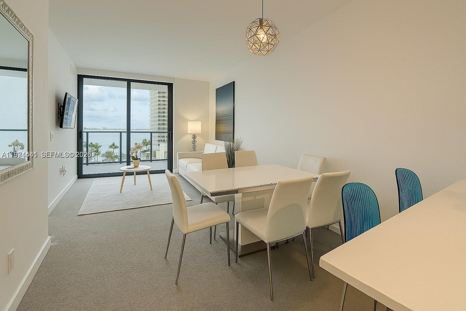 A dining area and living space feature a balcony with water views and modern furniture — 501 NE 31st St # 1204, Miami FL 33137, MIAMI, FL
