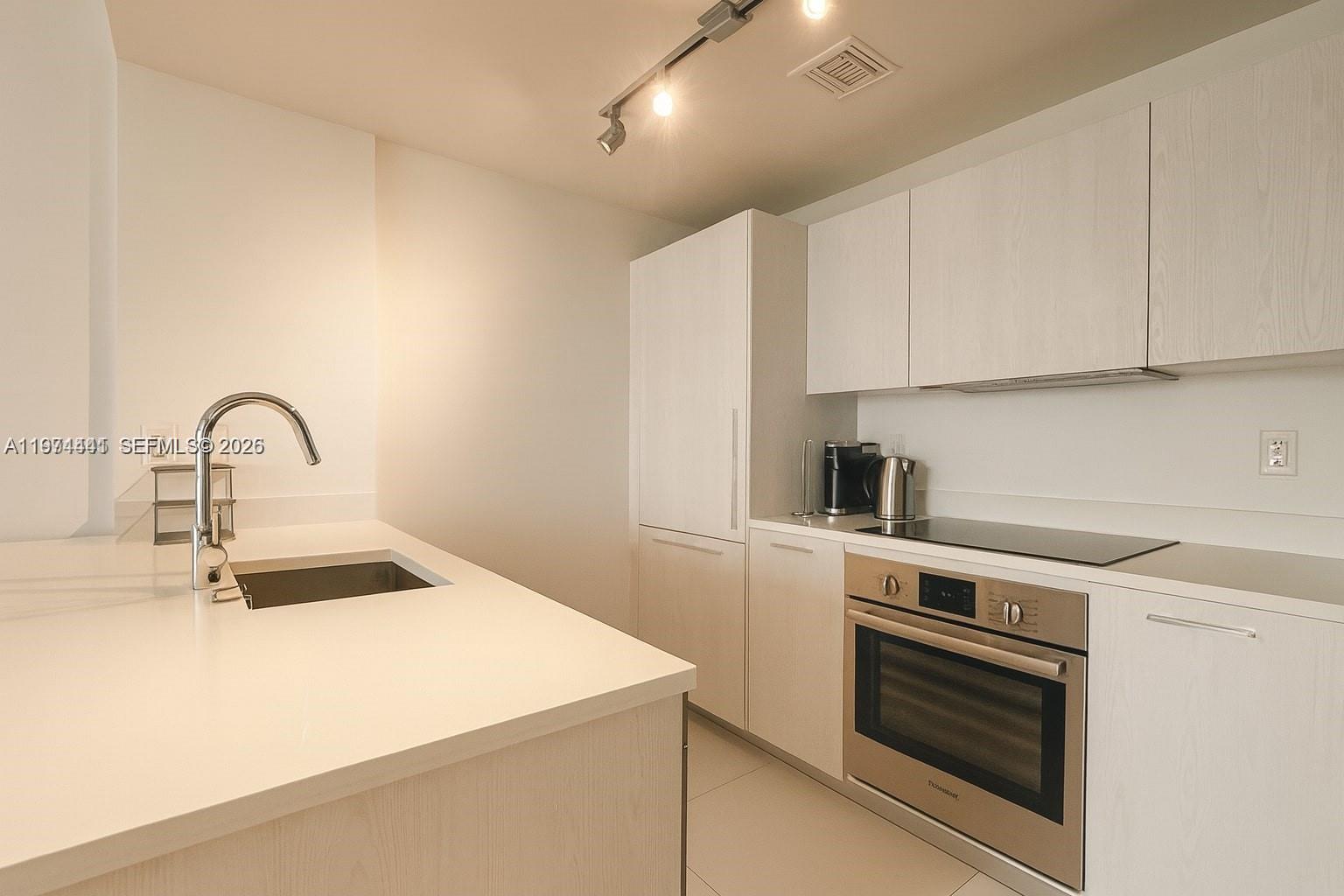 A modern kitchen features white cabinetry, stainless steel appliances, and a white countertop island — 501 NE 31st St # 1204, Miami FL 33137, MIAMI, FL