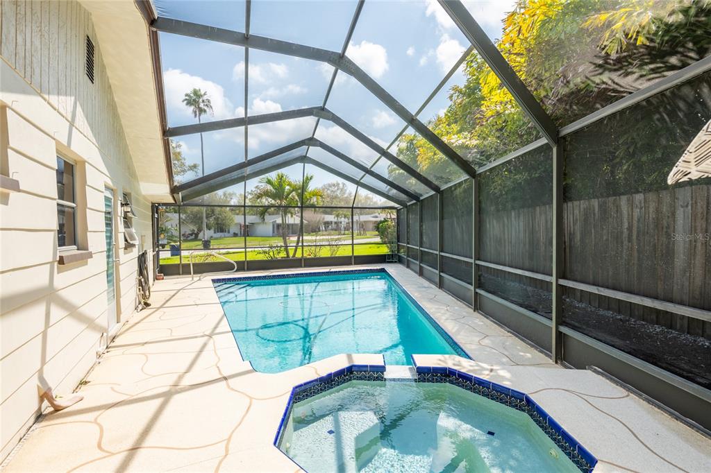A screened-in pool and hot tub area with a beige patio and a wooden fence — 1830 OAK FOREST DRIVE S, CLEARWATER, FL
